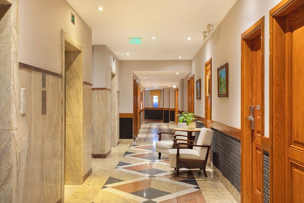 A hotel corridor with marble walls, a patterned floor, wooden doors, and a seating area with a plant. - Windsor Guanabara Hotel (Rio de Janeiro)
