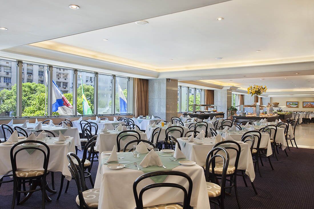 A dining area with tables set for a meal, large windows, and flags outside.