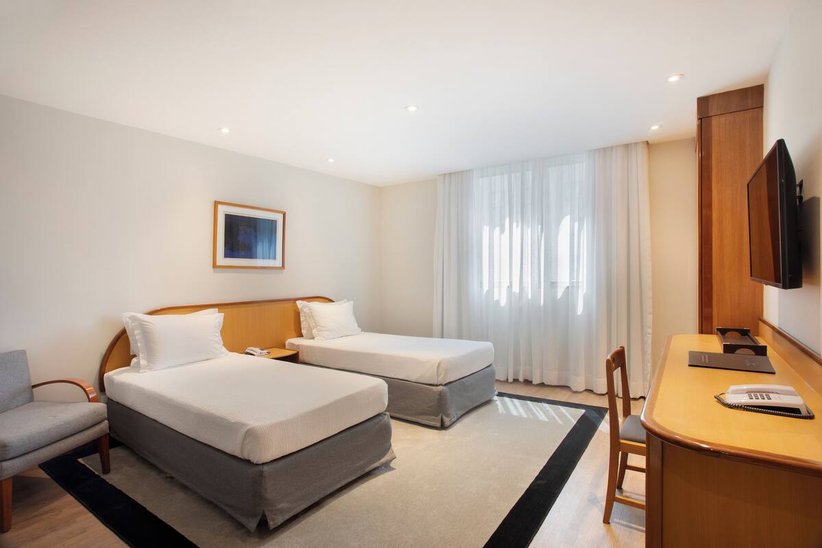 Hotelkamer met twee bedden, een bureau, een stoel, een televisie en een raam met gordijnen.