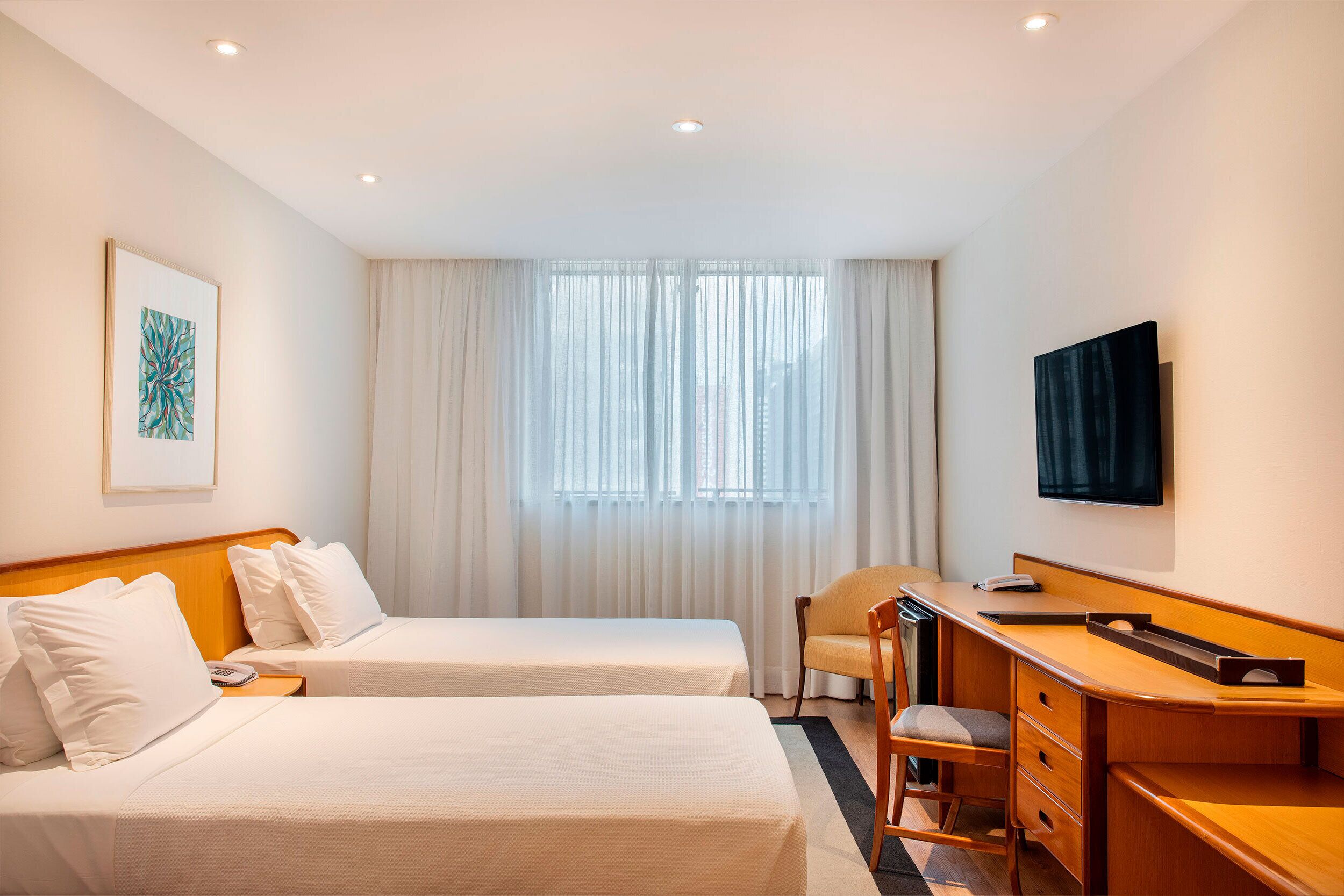 Une chambre d’hôtel avec deux lits, un bureau, une chaise, une télévision et une fenêtre avec des rideaux.
