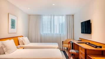 A hotel room with two beds, a desk, a chair, a television, and a window with curtains.