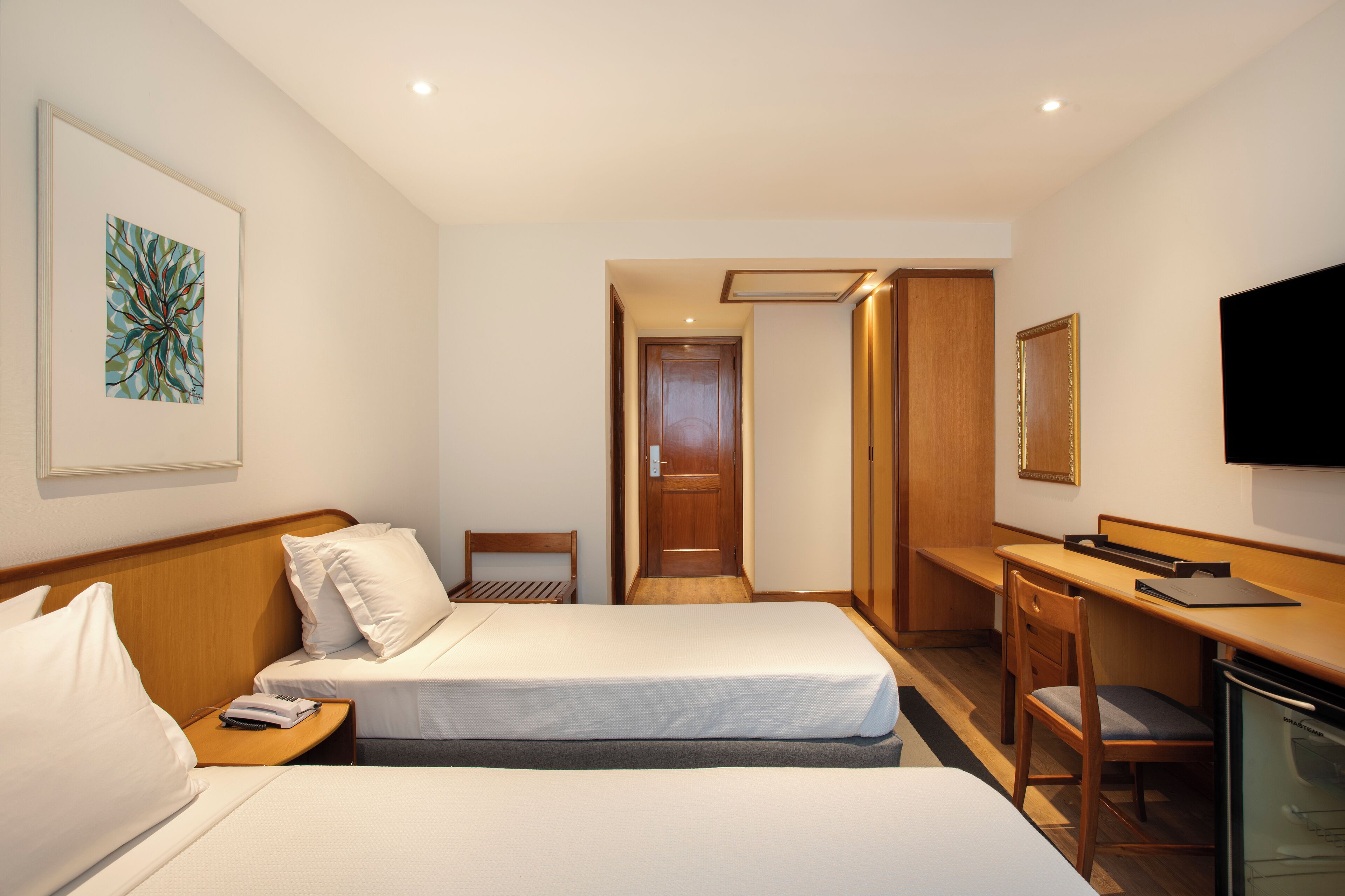A hotel room with two beds, a desk, a chair, a television, and a door leading to another room.