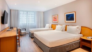 A hotel room with two beds, a desk, a chair, a TV, and two framed pictures on the wall. - Windsor Guanabara Hotel (Rio de Janeiro)