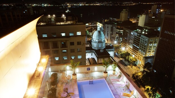 A rooftop pool area with lounge chairs and a large building with a dome in the background. - Windsor Guanabara Hotel (Rio de Janeiro)