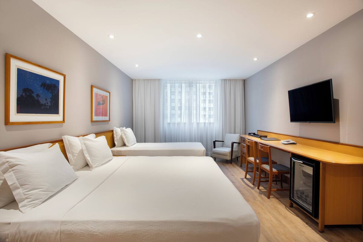 Hotelkamer met twee bedden, een bureau, een stoel, een televisie en een raam met gordijnen.