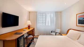 Une chambre d’hôtel avec un lit, un bureau avec un ordinateur, une télévision, une chaise et une fenêtre avec des rideaux.