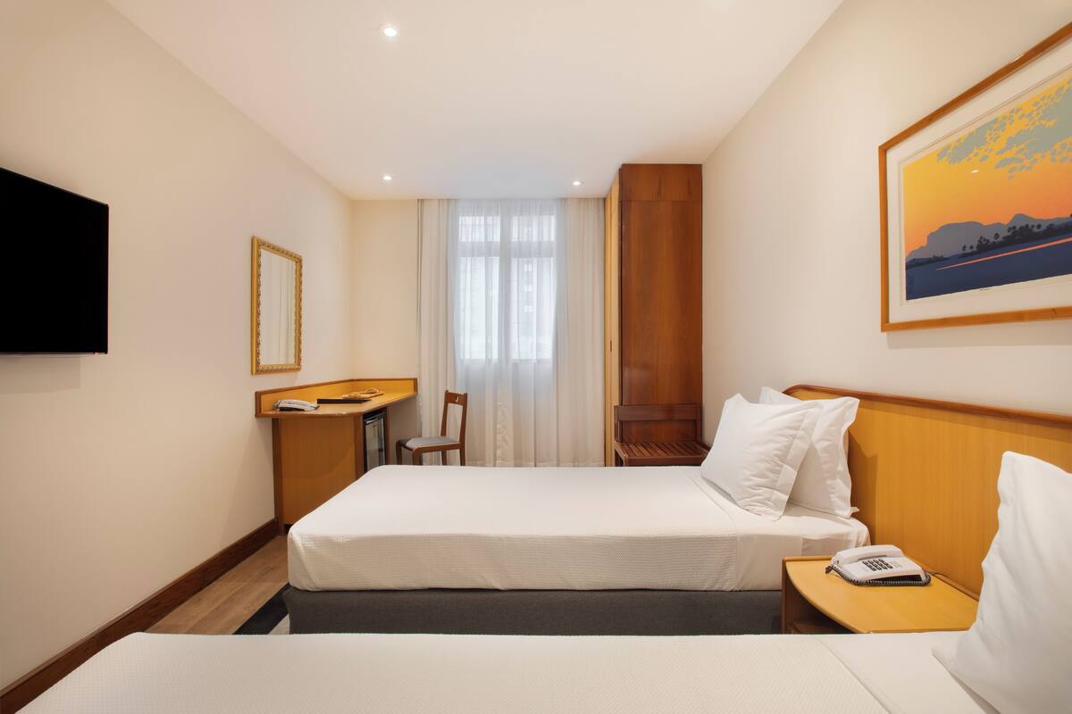Een hotelkamer met een bed, een bureau, een stoel, een televisie en een schilderij aan de muur.