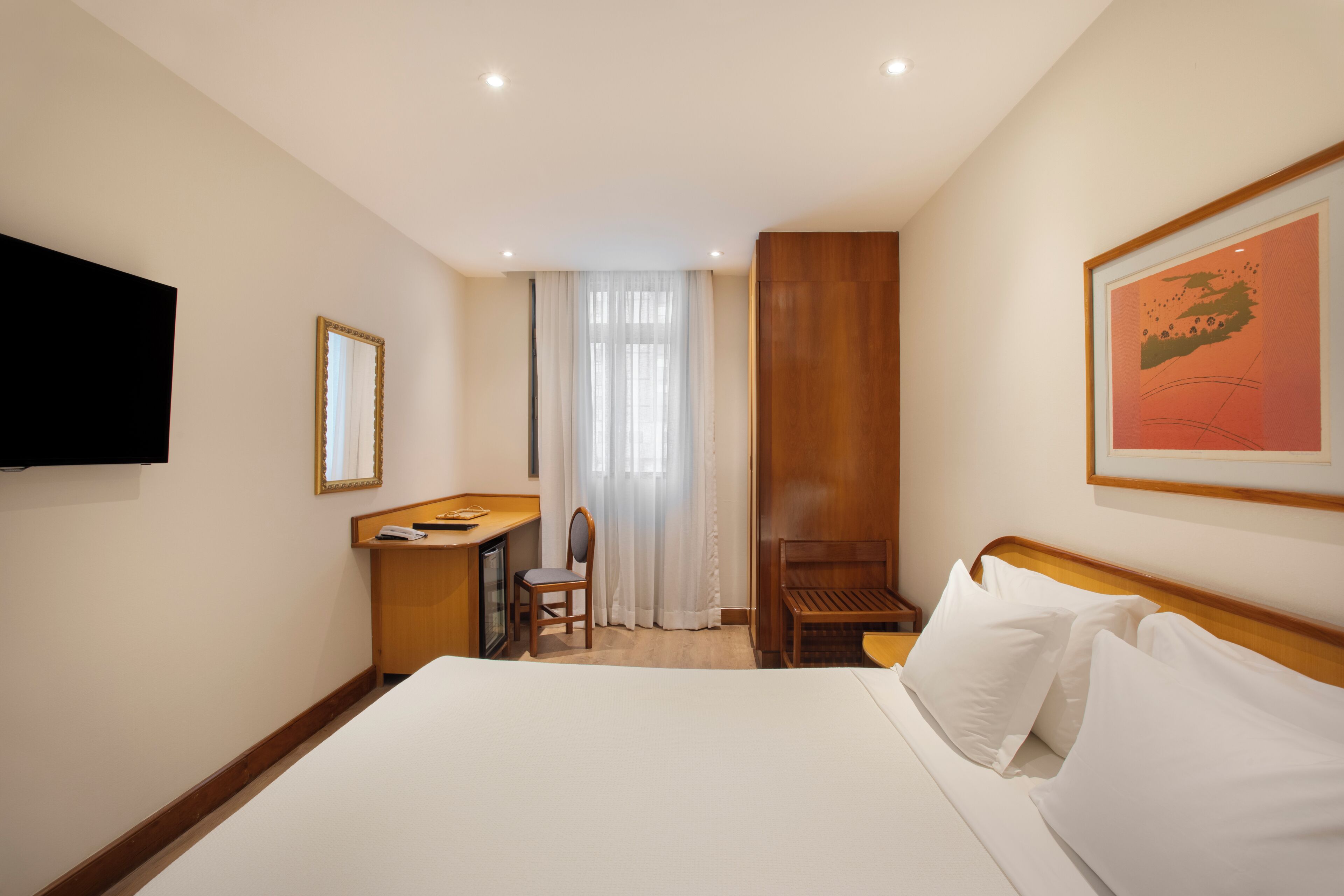 A hotel room with a bed, a desk, a chair, a television, and a window with curtains.