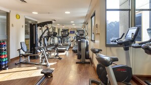 Un gimnasio con diversas máquinas de ejercicio, suelo de madera y amplios ventanales que ofrecen vistas de la ciudad.