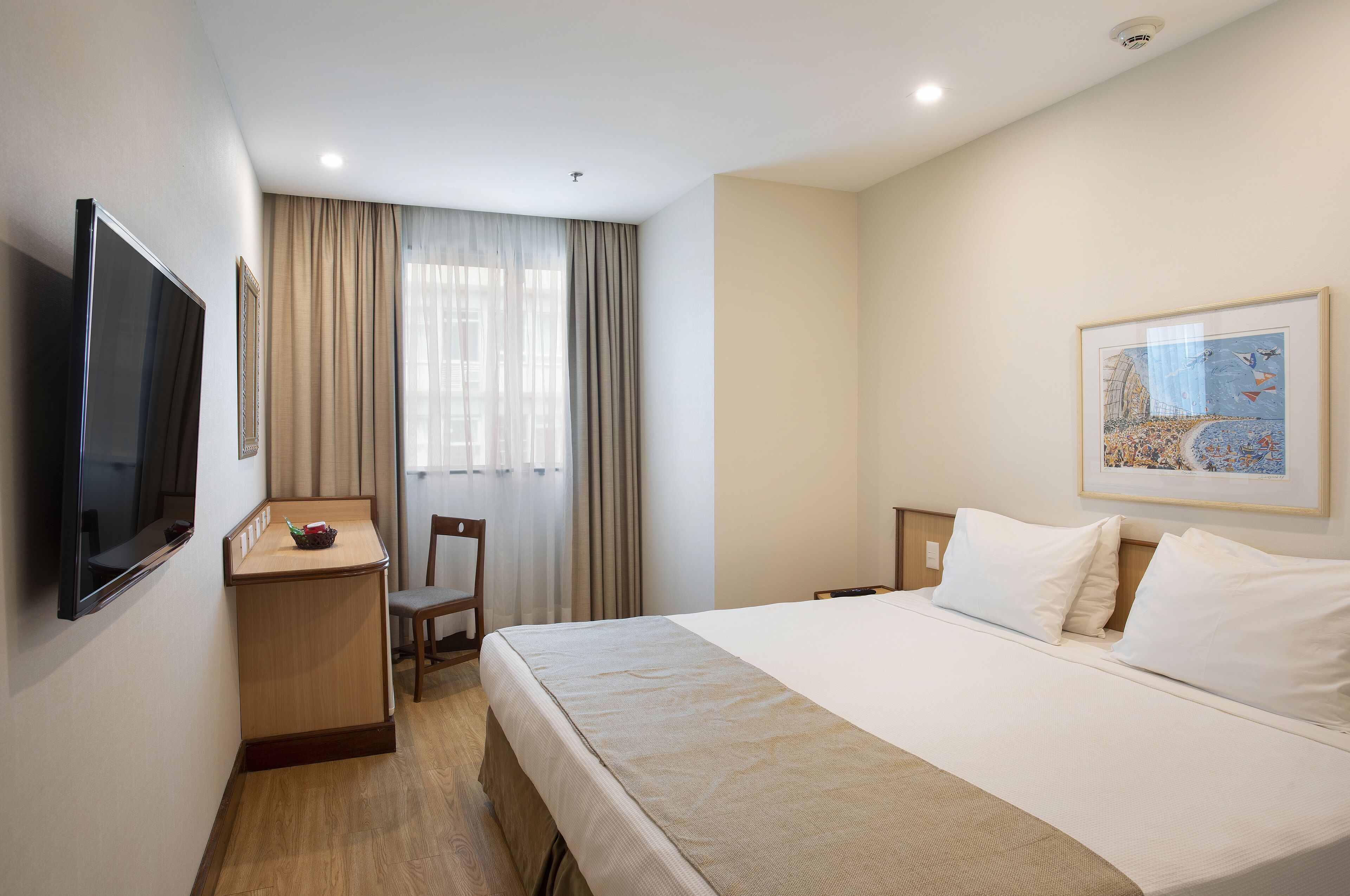 A hotel room with a bed, a desk, a chair, a television, and a window with curtains.