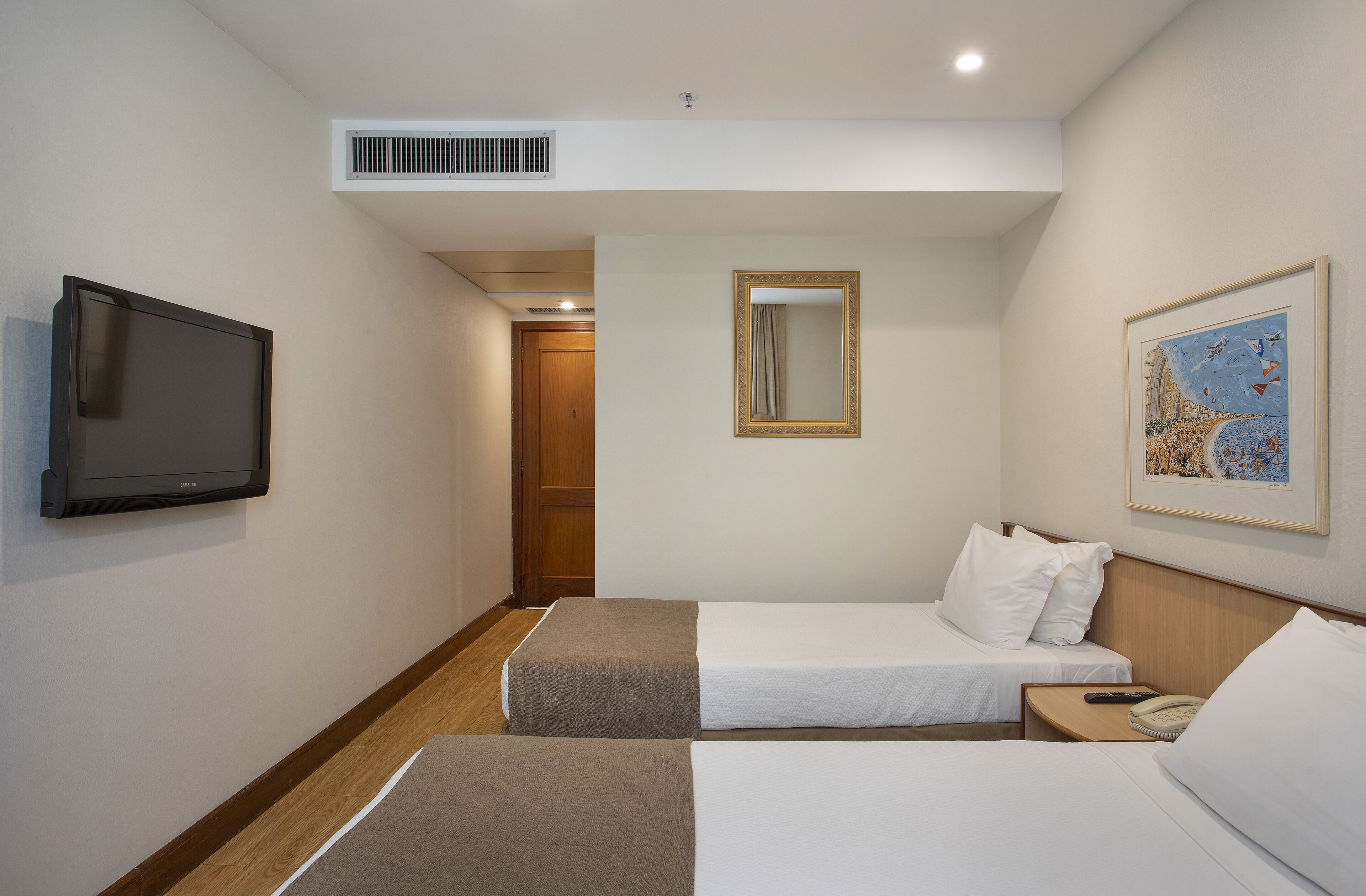 Ein Hotelzimmer mit zwei Betten, einem Fernseher, einem Spiegel und einem Bild an der Wand.
