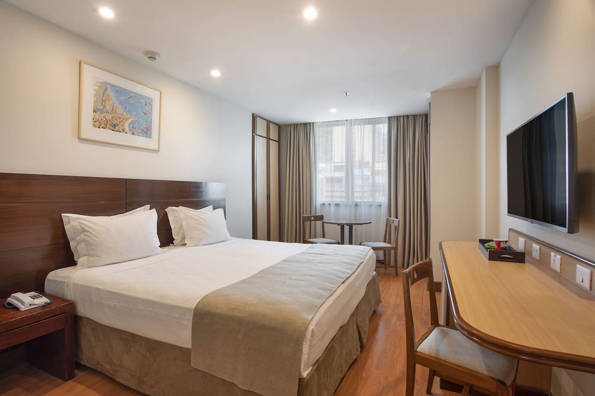 Une chambre d’hôtel avec un grand lit, un bureau, une chaise, une télévision et un tableau au mur.