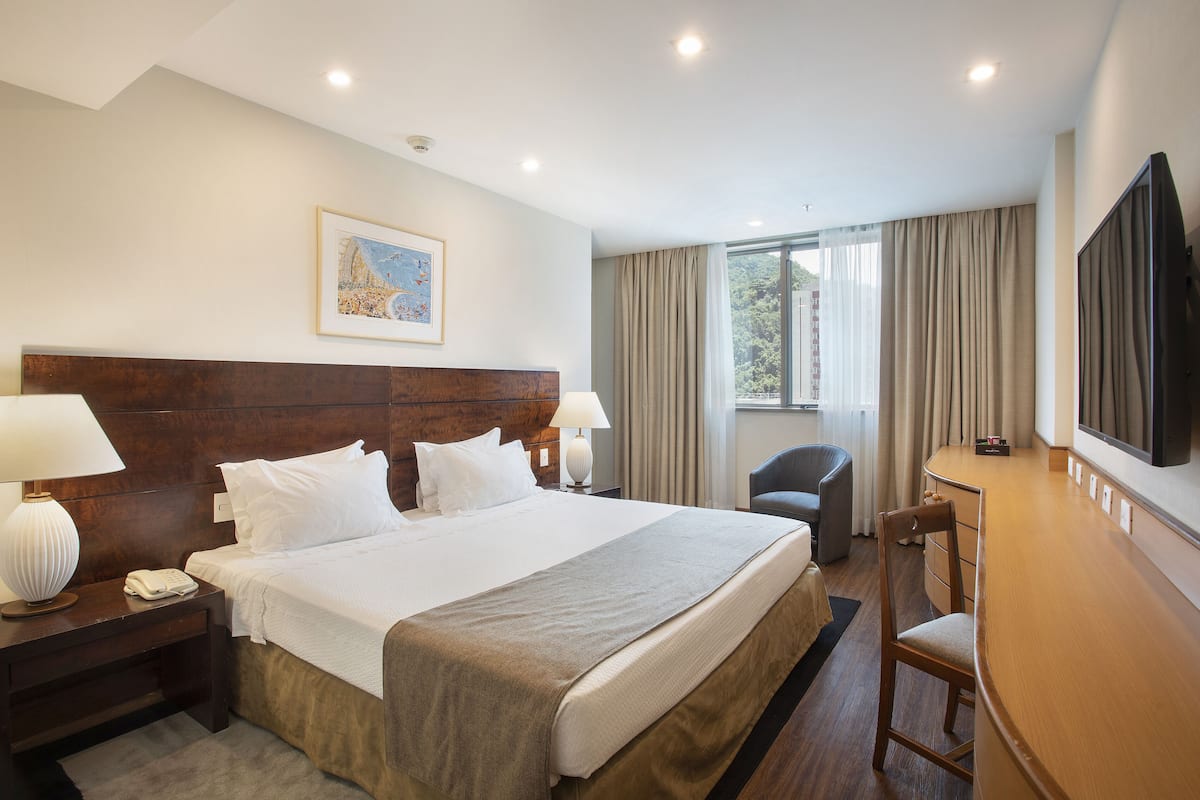 Une chambre d’hôtel avec un grand lit, un bureau, une chaise, une télévision et une fenêtre avec des rideaux.