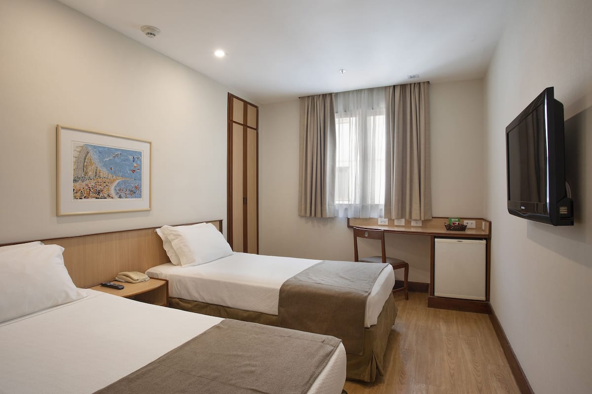 Une chambre d’hôtel avec deux lits, un bureau, une télévision et un tableau au mur.
