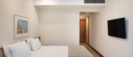 A hotel room with a bed, a flat-screen TV mounted on the wall, a framed picture on the wall, and a door leading to another room.