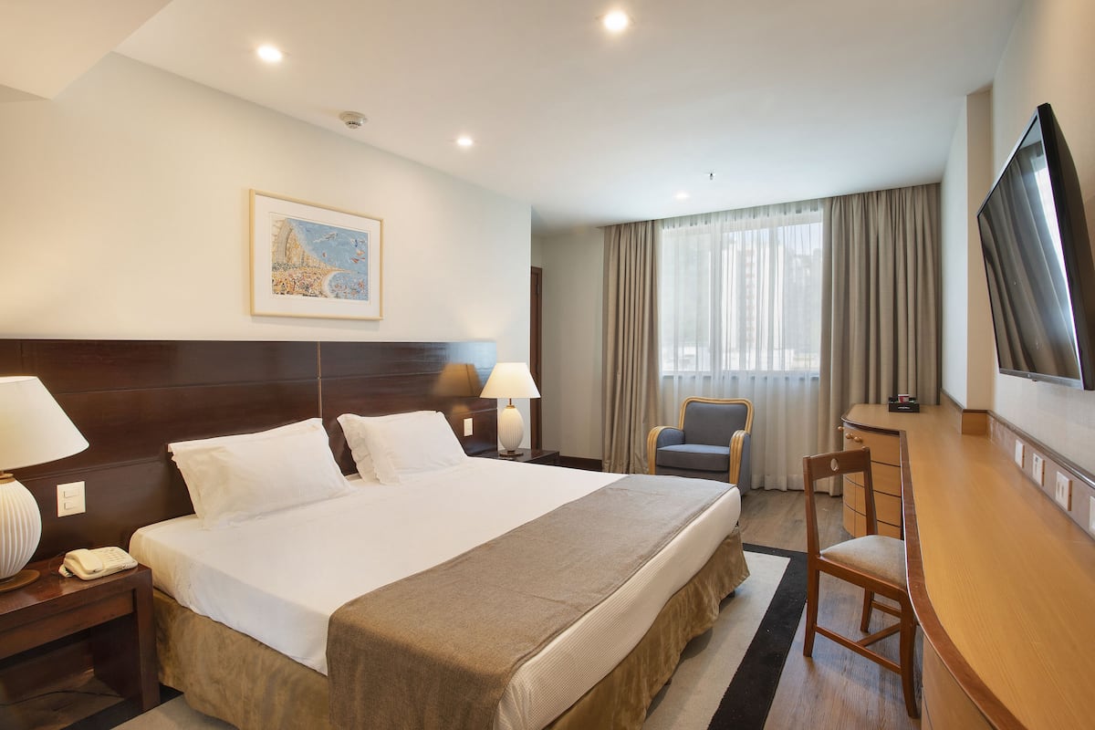 Une chambre d’hôtel avec un grand lit, des lampes de chevet, un bureau avec une chaise, une télévision et une fenêtre avec des rideaux.