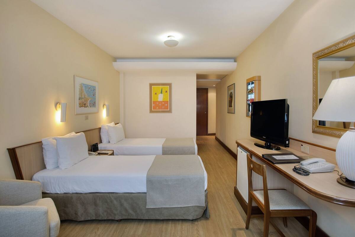 Une chambre d ’hôtel avec deux lits, un bureau avec un ordinateur, une télévision et un miroir.