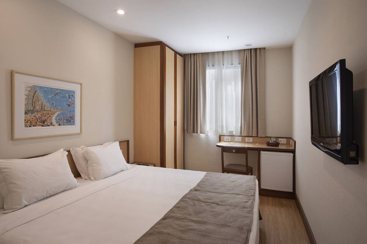 Une chambre d’hôtel avec un lit, un bureau, une télévision et un tableau au mur.