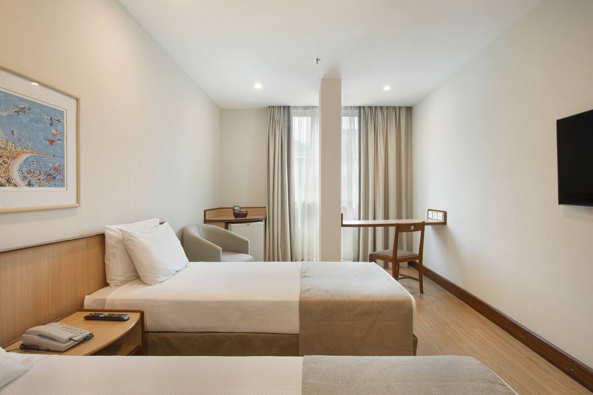 Une chambre d’hôtel équipée d’un lit, d’une table de chevet, d’une chaise, d’un bureau et d’un téléviseur fixé au mur.