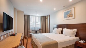 Habitación de hotel con cama, mesita de noche, televisor, mesa de comedor, sillas y un cuadro en la pared.