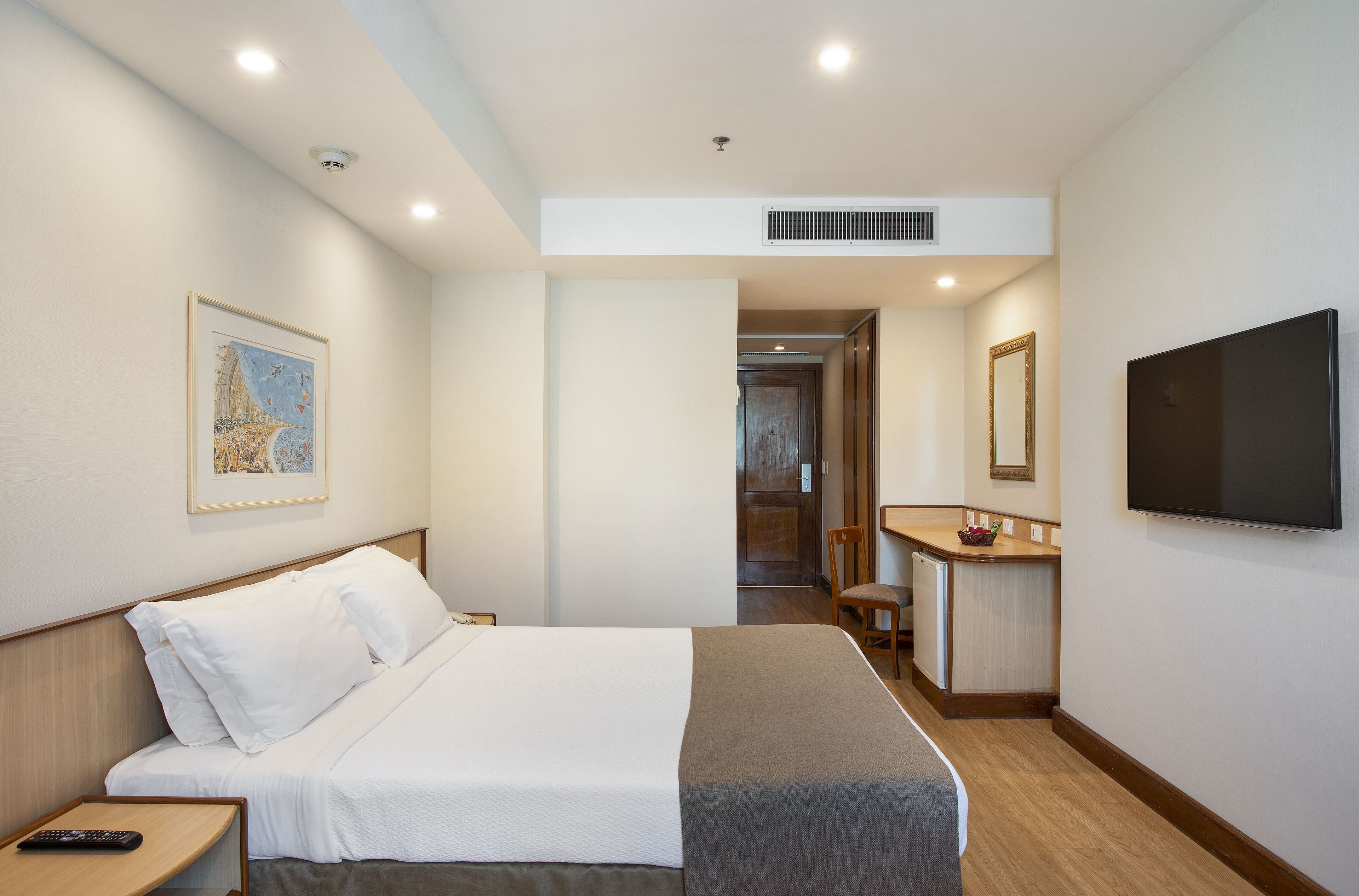 A hotel room with a bed, a desk, a chair, a television, and a framed picture on the wall.