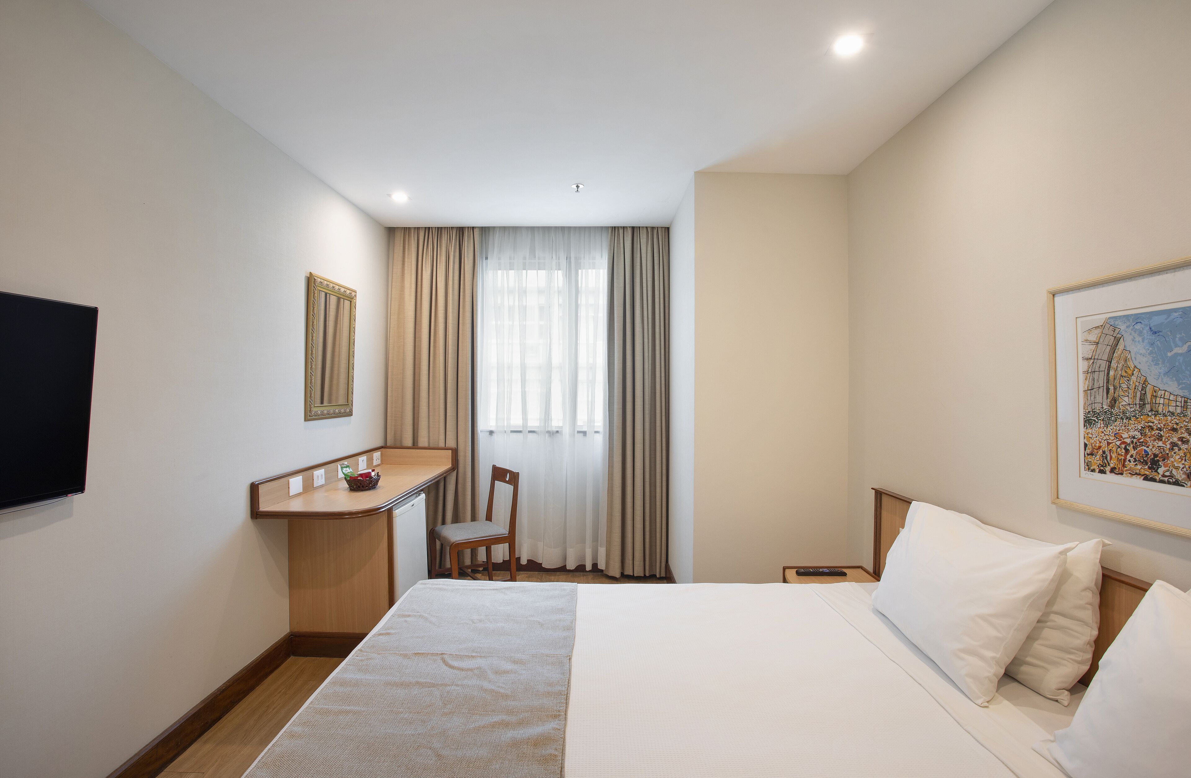 Habitación de hotel con cama, escritorio, silla, televisión y ventana con cortinas.