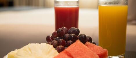 A plate with pineapple, watermelon, and grapes, and two glasses of juice.