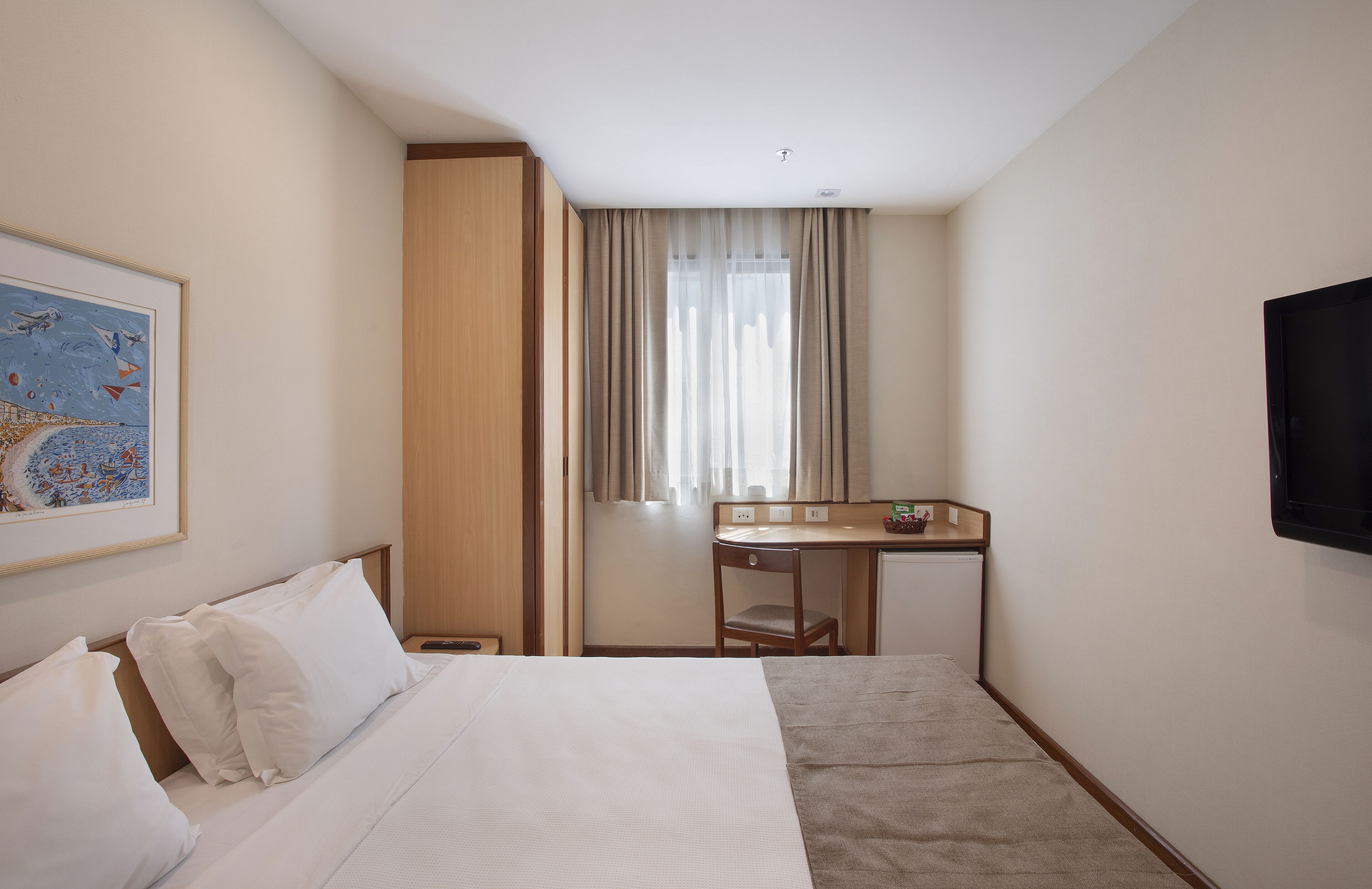 A hotel room with a bed, a desk, a chair, a television, and a window with curtains.