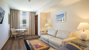 Habitación de hotel con sofá, dos sillones, una mesita, una lámpara y un cuadro en la pared.
