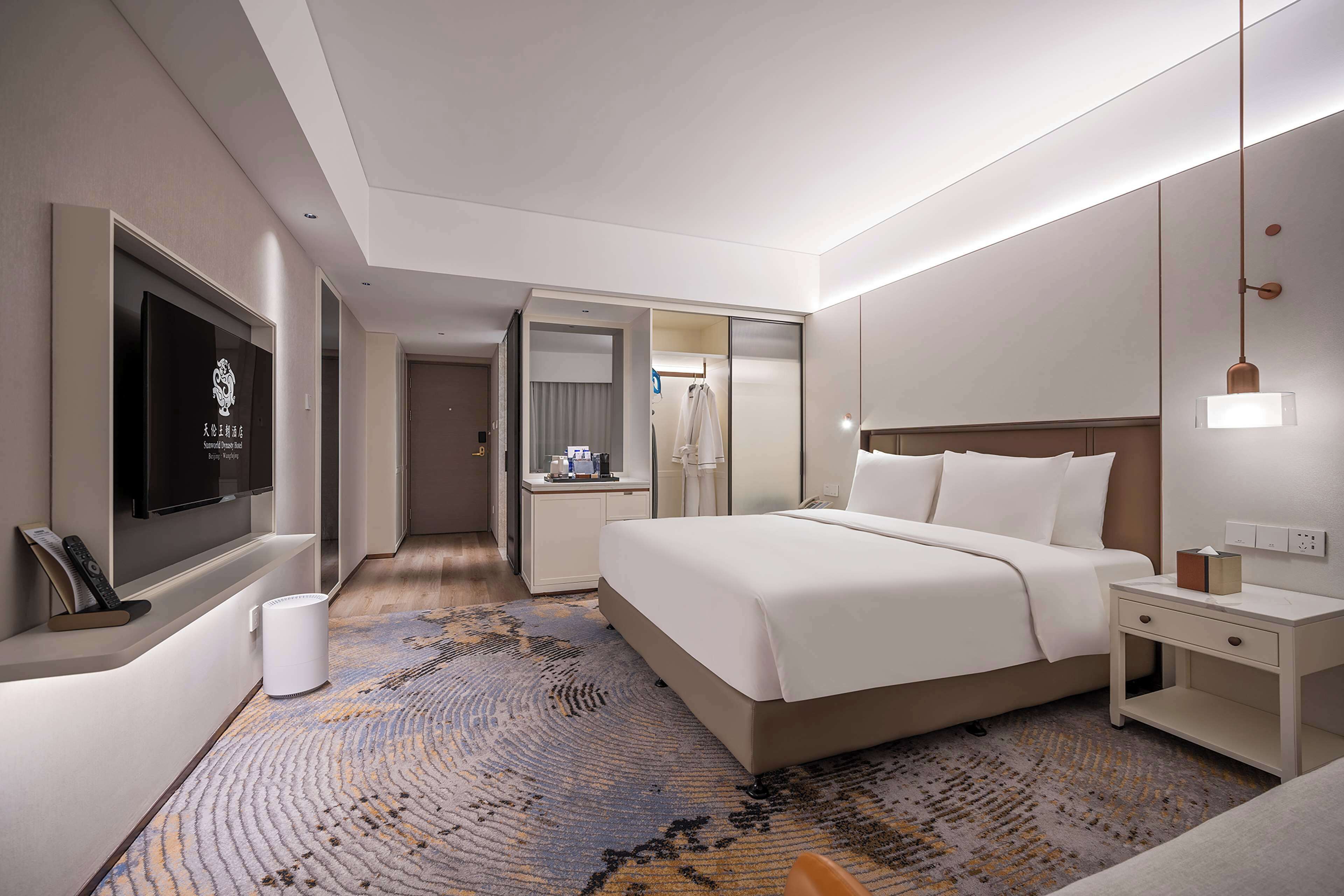 A modern hotel room with a large bed, bedside tables, a TV, and a bathroom with a mirror and towel rack.