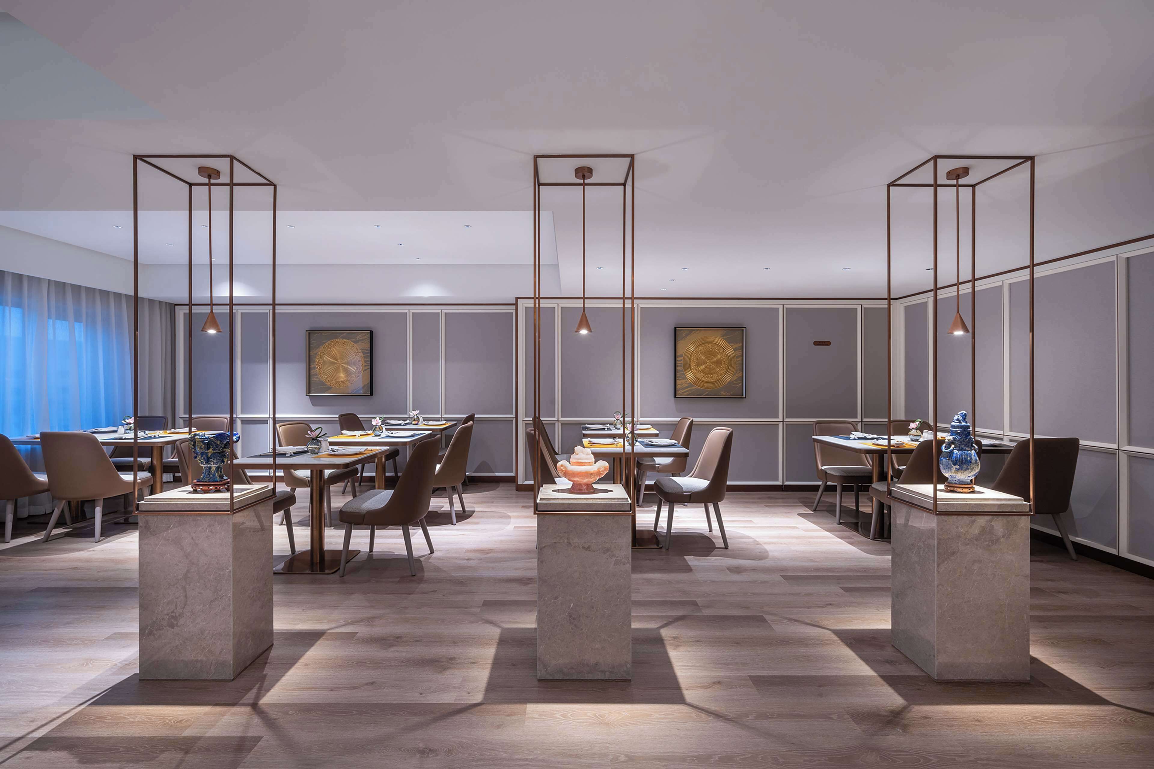 Un espace de restauration moderne, avec des tables et des chaises, des luminaires suspendus et des vases décoratifs posés sur des piédestaux.