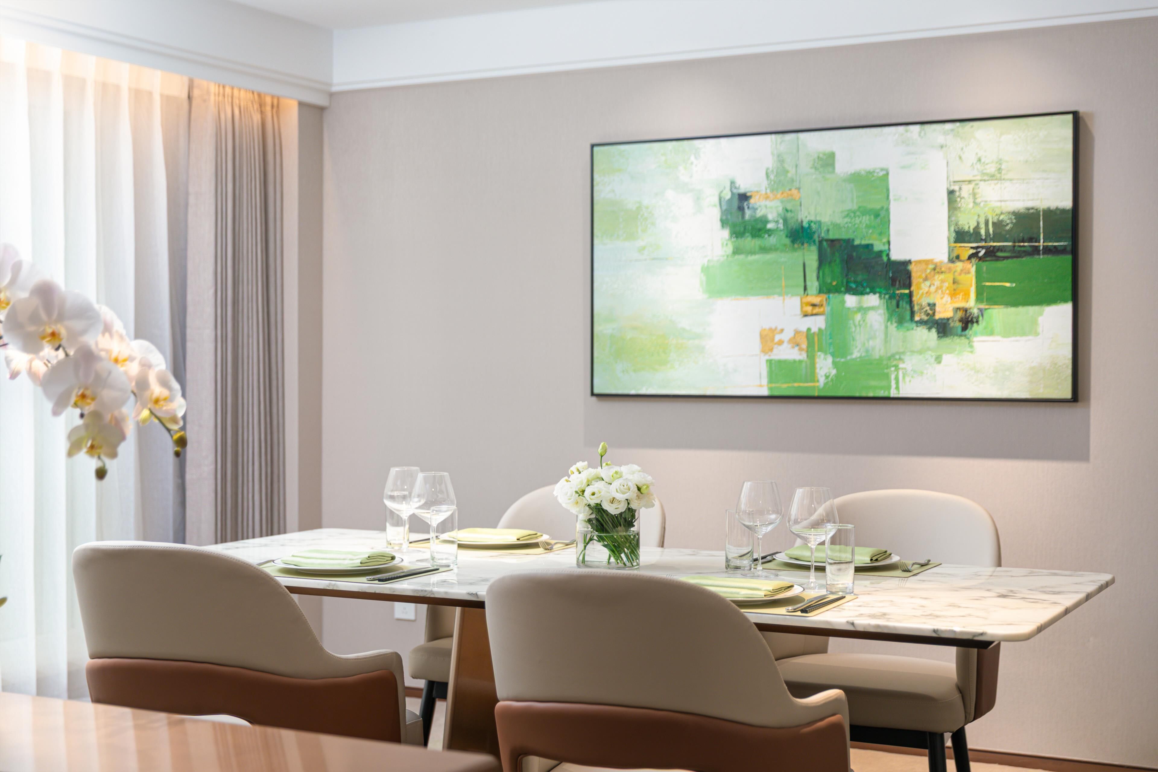 Un comedor con una mesa lista para dos, un jarrón con flores blancas y un cuadro abstracto grande en la pared.