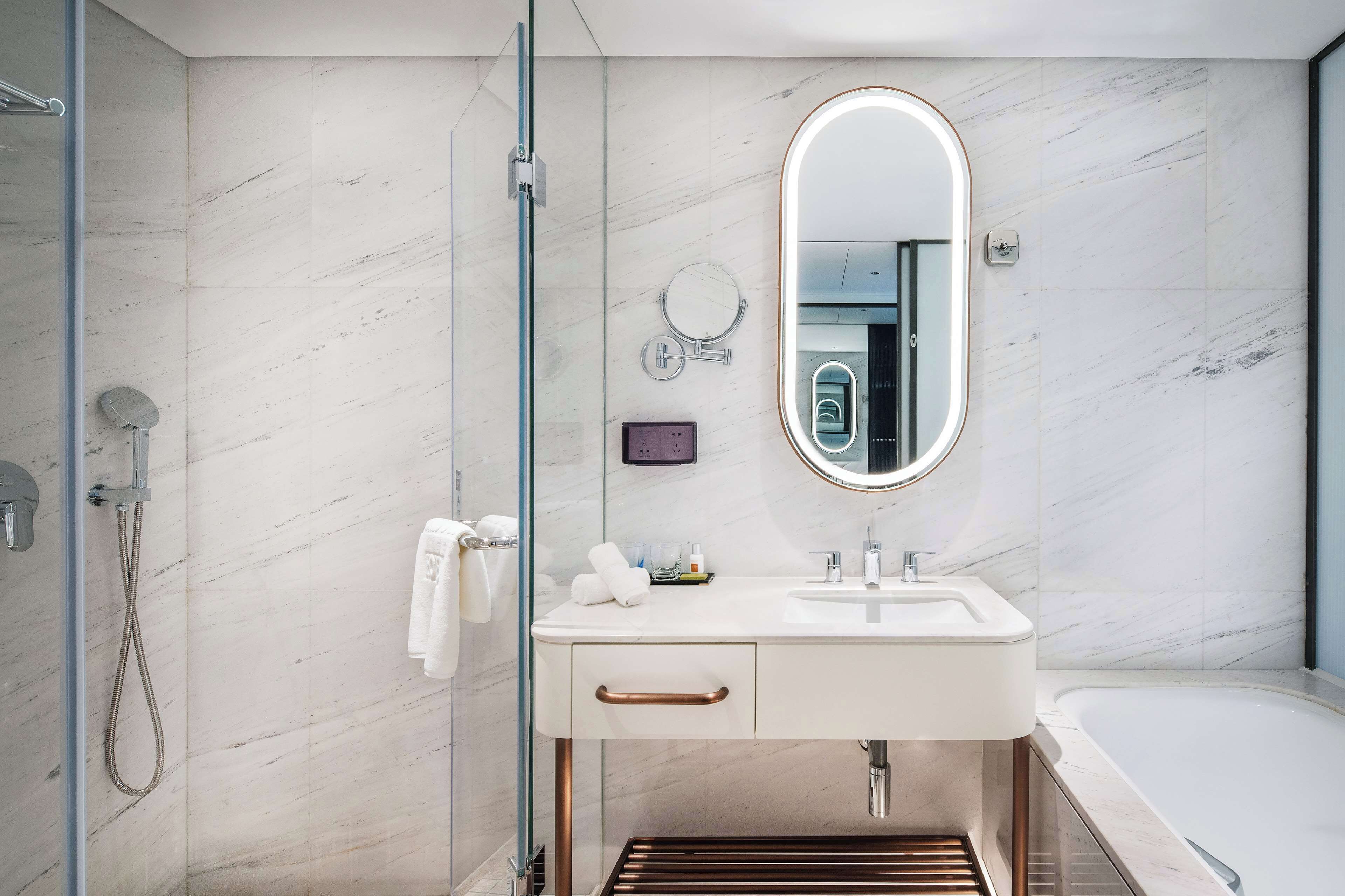 A modern bathroom with a glass shower enclosure, a white sink with a mirror above it, and a bathtub.