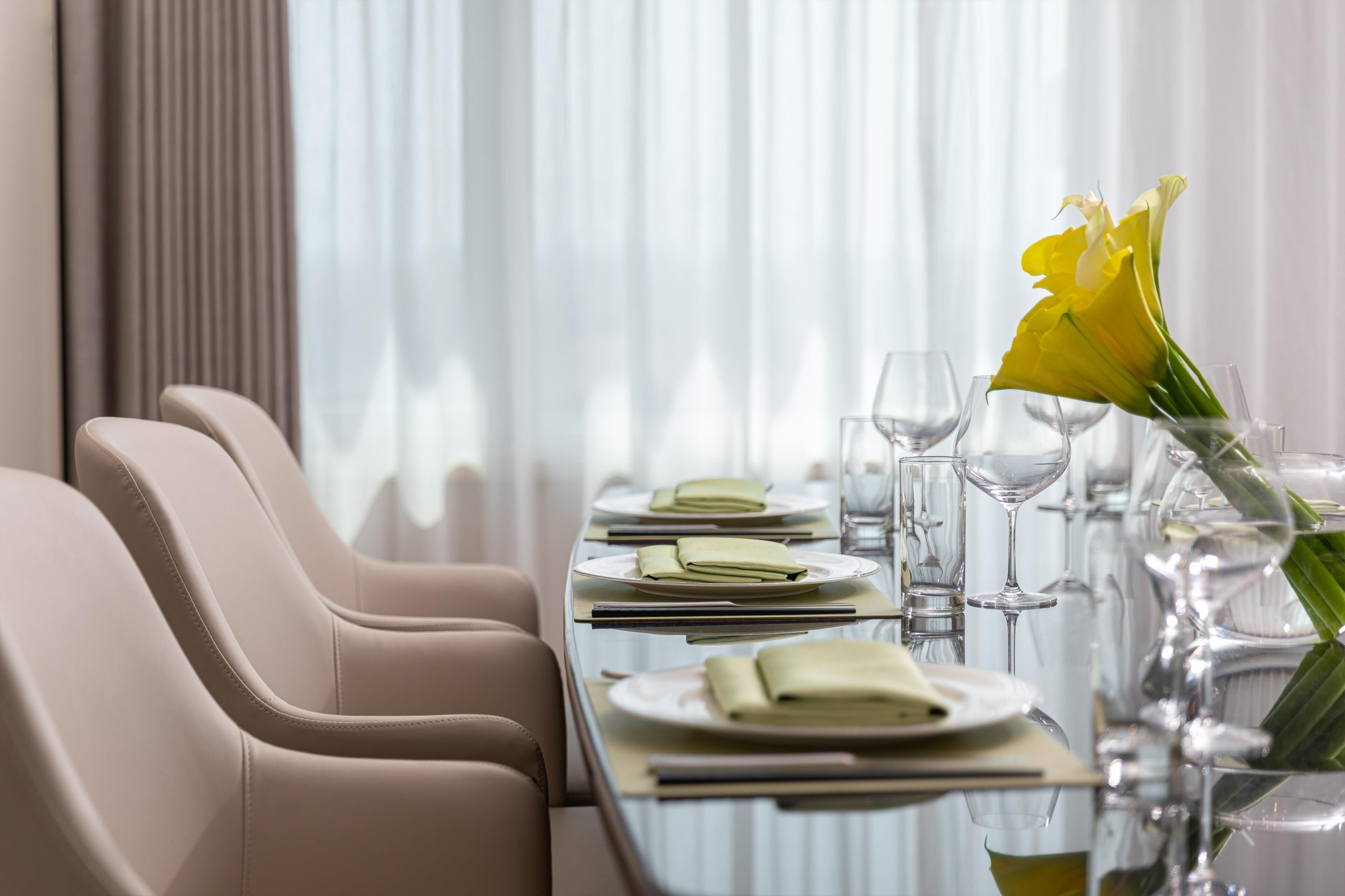 Una mesa de comedor dispuesta con platos, vasos y un jarrón de flores.