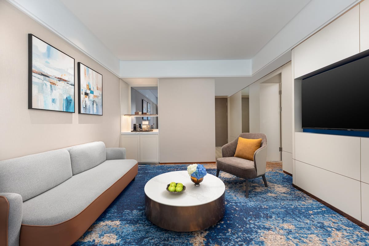 A modern living room with a sofa, armchair, coffee table, and artwork on the walls.