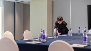 Una sala de conferencias con una larga mesa, sillas, botellas de agua y una persona sentada a la mesa.
