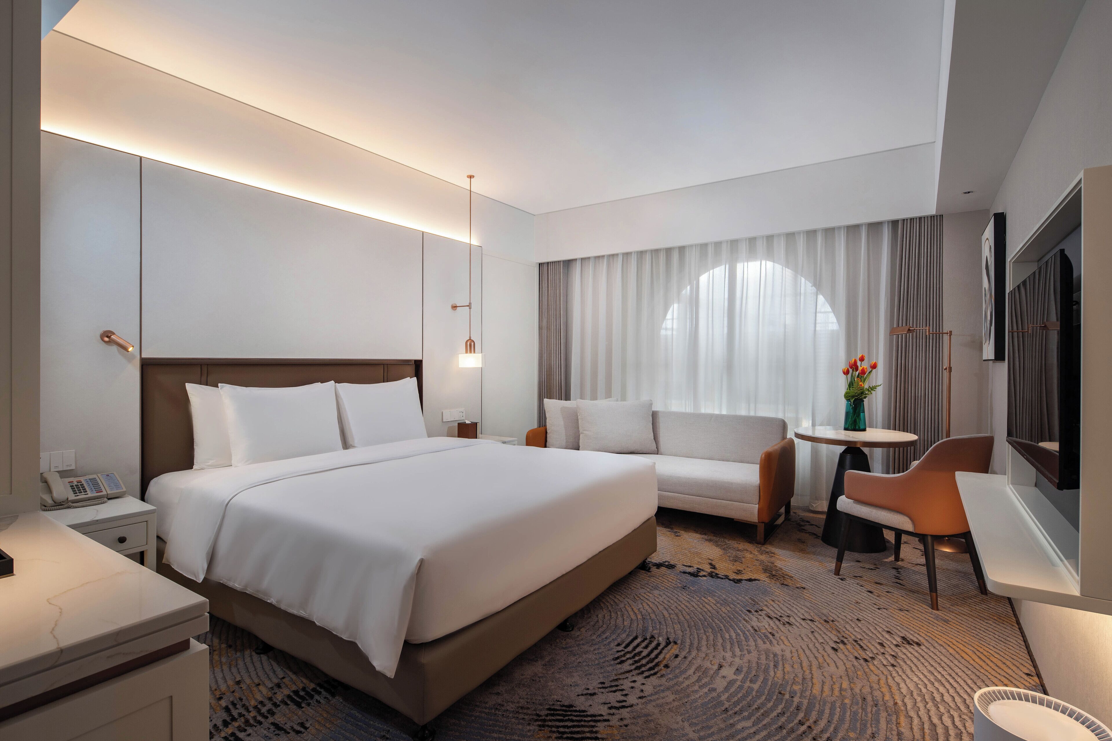 A hotel room with a large bed, a sofa, a small table, and a chair.