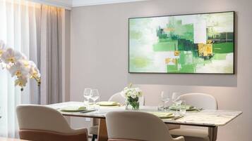 Un comedor con una mesa preparada para cuatro personas, un jarrón de flores blancas y un cuadro abstracto grande en la pared.