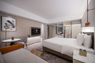 Una habitación de hotel moderna con una cama, un sofá, una mesita, una silla, un televisor y un espejo.