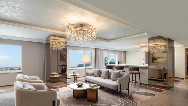 Ein modernes Hotelzimmer mit Sofa, Sesseln, einem Essbereich und einem großen Fenster mit Blick auf die Stadt.