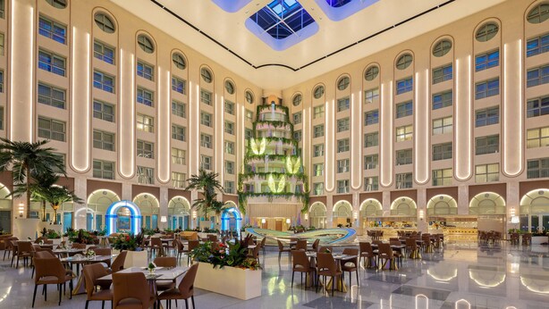 A spacious hotel lobby with a central atrium, multiple dining areas, and a distinctive vertical garden feature.
