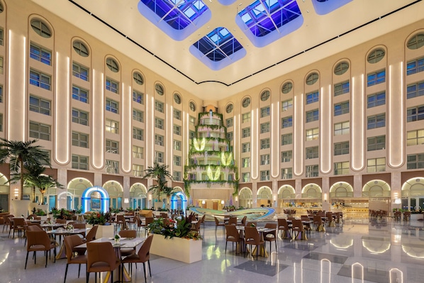 Un amplio vestíbulo de hotel con un atrio central, varias zonas de comedor y un llamativo jardín vertical.