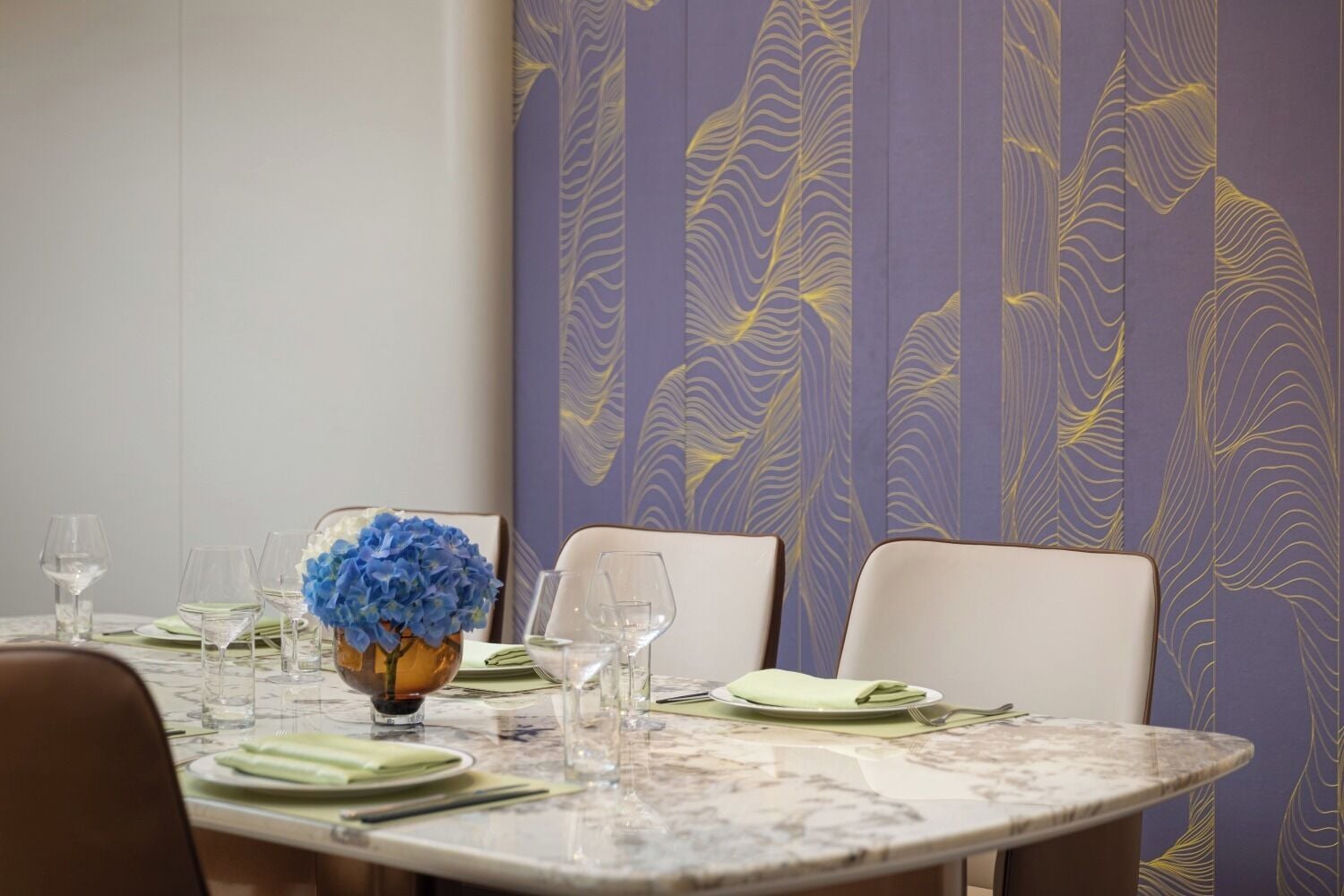 A dining table set with plates, glasses, and a vase of blue flowers.