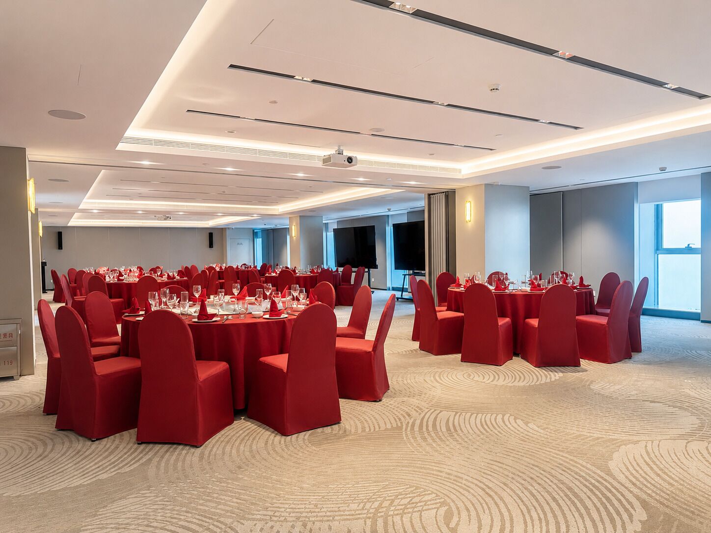 Un salón de conferencias con mesas redondas, sillas rojas y suelo alfombrado.