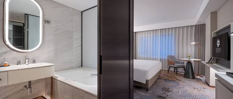 Una habitación de hotel moderna con baño, cama, televisor y escritorio.