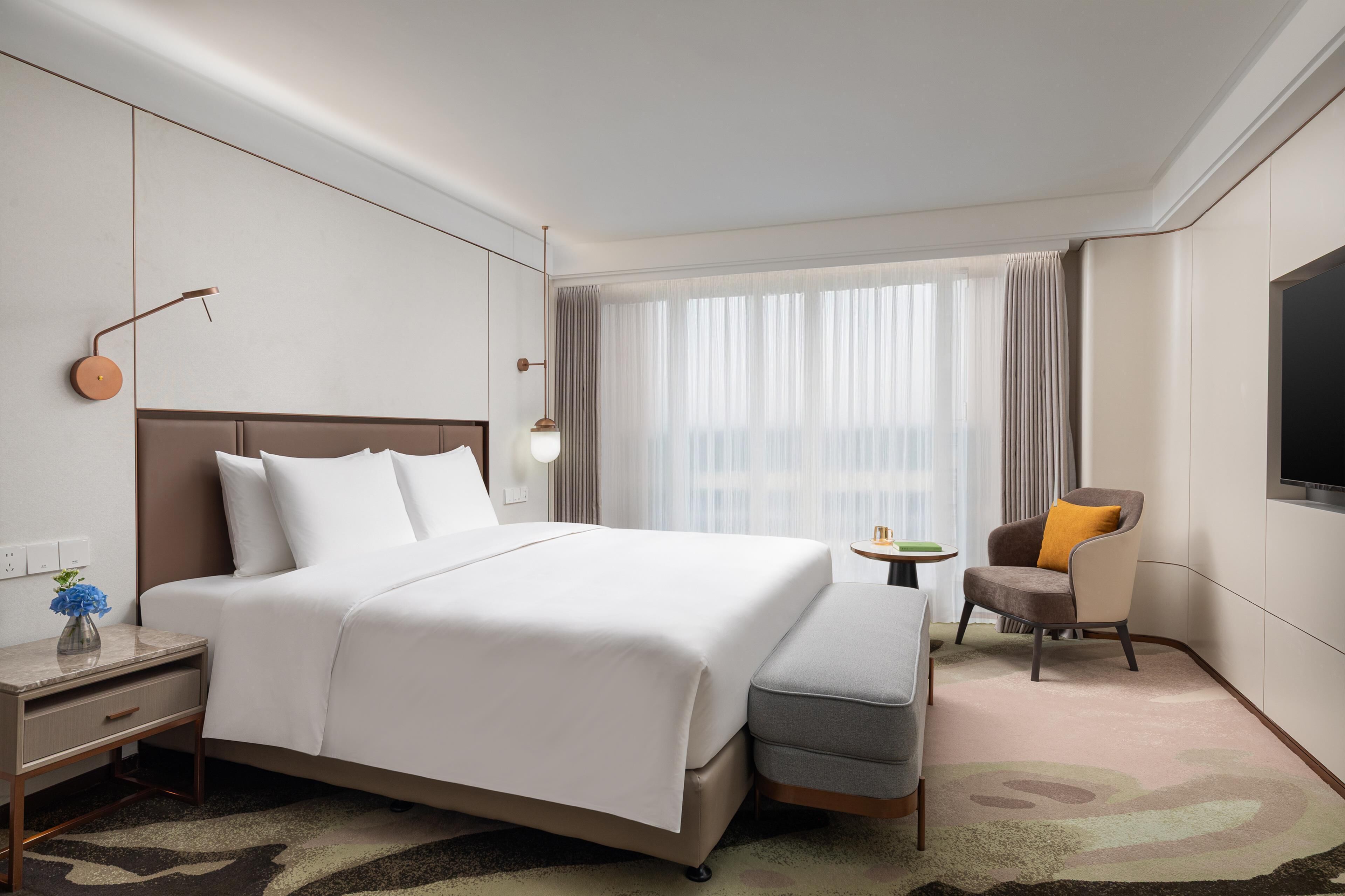 Une chambre d’hôtel avec un grand lit, un bureau avec une lampe, une chaise et un téléviseur fixé au mur.