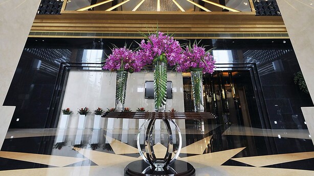 A modern lobby with a geometric floor pattern, a central light fixture, and a reception desk.
