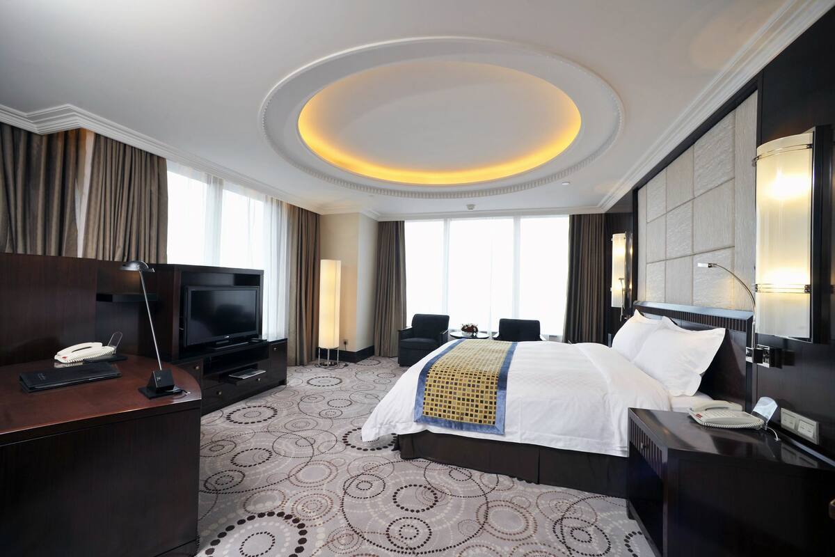Habitación de hotel con una cama grande, un escritorio con televisor de pantalla plana, una lámpara de escritorio, un teléfono y una mesita de noche con lámpara.