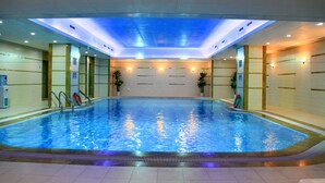 An indoor swimming pool with clear water, surrounded by walls with tiled patterns and potted plants.