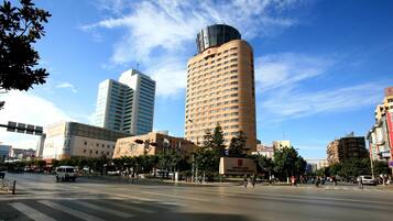 A modern urban street with tall buildings, including a prominent hotel with a cylindrical tower and a flat-roofed building with a large sign.